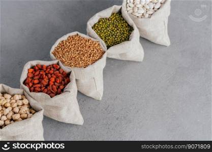 Assorted gluten free grains in linen cloth bags on grey background. Sacks filled with kidney bean, lentil, buckwheat, goji and garbanzo. Cereals for healthy eating