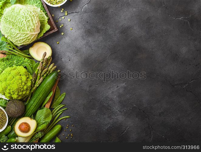 Assorted green toned raw organic vegetables on dark background. Avocado, cabbage, broccoli, cauliflower and cucumber with trimmed beans.