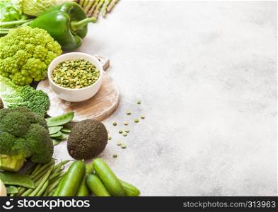 Assorted green toned raw organic vegetables on white background. Avocado, cabbage, broccoli, cauliflower and cucumber with trimmed beans and split peas in white bowl. Space for text