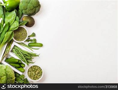 Assorted green toned raw organic vegetables on white background. Avocado, cabbage, broccoli, cauliflower and cucumber with trimmed mung beans and split peas in white bowl.