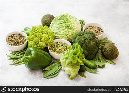 Assorted green toned raw organic vegetables on white background. Avocado, cabbage, broccoli, cauliflower and cucumber with trimmed and mung beans, pak choi, loose pepper and lettuce