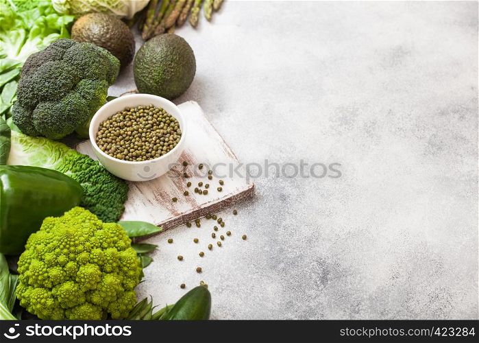 Assorted green toned raw organic vegetables on white background. Avocado, cabbage, broccoli, cauliflower and cucumber with trimmed mung beans in white bowl and loose pepper. Space for text