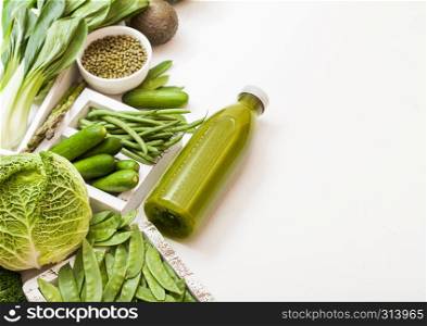 Assorted green toned raw organic vegetables on white stone background. Avocado, cabbage, cauliflower and cucumber with trimmed and mung beans and bottle of smoothie.