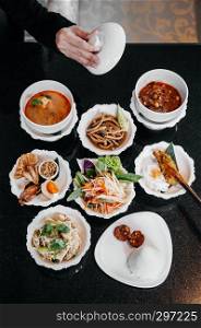 Assorted Traditional Thai food, red Massaman curry, Tom Yum spicy soup, Papaya salad, Grilled chicken and local dishes on black table top view shot