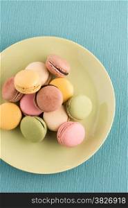 Assortment of gentle colorful macaroons on green ceramic plate on blue placemat background.