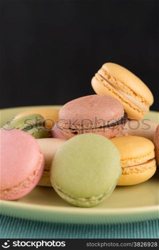 Assortment of gentle colorful macaroons on green ceramic plate on blue placemat background.
