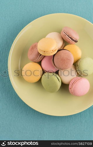 Assortment of gentle colorful macaroons on green ceramic plate on blue placemat background.