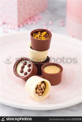 Assortment of luxury white and dark chocolate candies variety on pink plate with cup and gift box