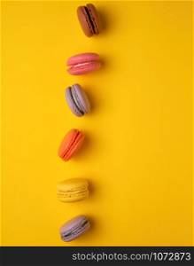 assortment of multi-colored baked round macarons on a yellow background, flat lay, copy space
