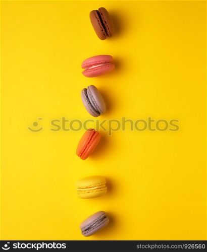 assortment of multi-colored baked round macarons on a yellow background, flat lay, copy space