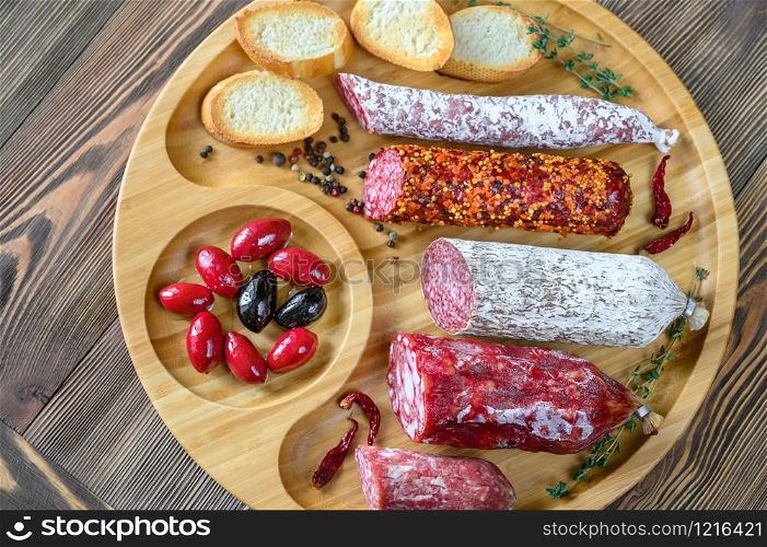 Assortment of salami with appetizers on wooden background: top view
