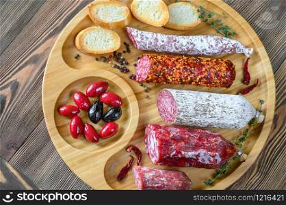 Assortment of salami with appetizers on wooden background: top view