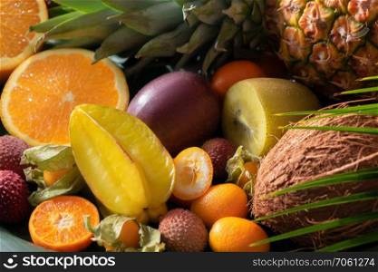 Assortment of tropical exotic fruits: halves of oranges, lychees, carambola, pineapple, lemon, physalis, coconut, lychee with leaves of palm close up. Fresh exotic organic fruits close up as natur background