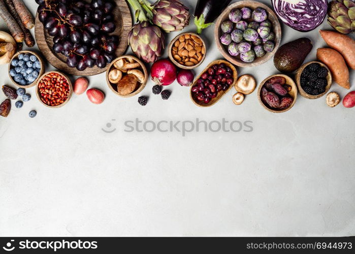 Assortment raw organic of purple ingredients: eggplants, artichokes, potatoes, onions, berries, nuts, carrots, brussel sprouts, grapes over gray concrete background. Top view with space. Food frame