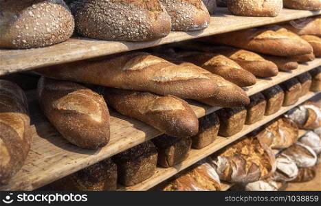 Assortments of bread, freshly baked on wooden shelves. Piles of breads. Bakery shelves full of breads. Bakery goods. Variety of loaves and buns.