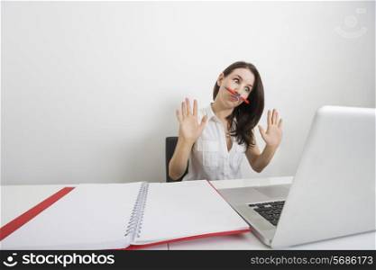 Astonished businesswoman looking at laptop while holding pen under nose in office