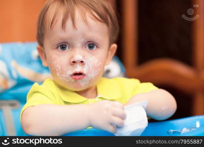 Astonished little boy wearing yellow t-shirt at home, face got dirty with yoghurt