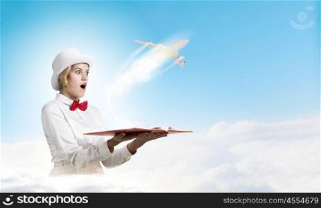 Astonished woman looking in book. Young woman in white hat with opened book in hands and airplane flying out