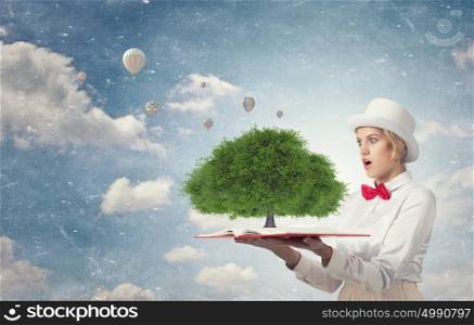 Astonished woman looking in book. Young woman in white hat with opened book in hands and green tree on pages