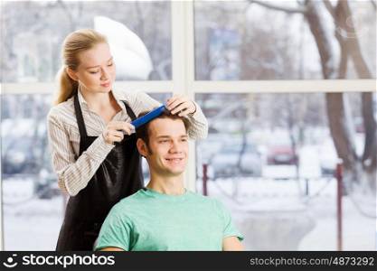 At beauty salon. Young man in chair at barbers and woman hairdresser