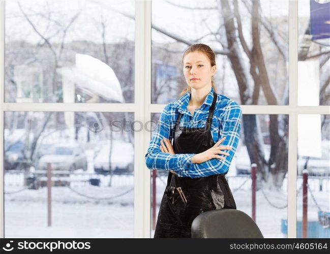 At beauty salon. Young woman hairdresser in apron standing near window