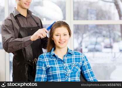 At beauty salon. Young woman in chair at barbers and male hairdresser