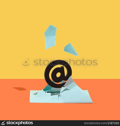 At, email sign, burst out of a blue envelope against orange and yellow background. Minimal concept. Square with copy space.. At, email sign, burst out of a blue envelope against orange and yellow background.