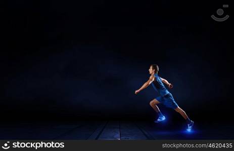 At full speed. Running man in blue sport wear on black background