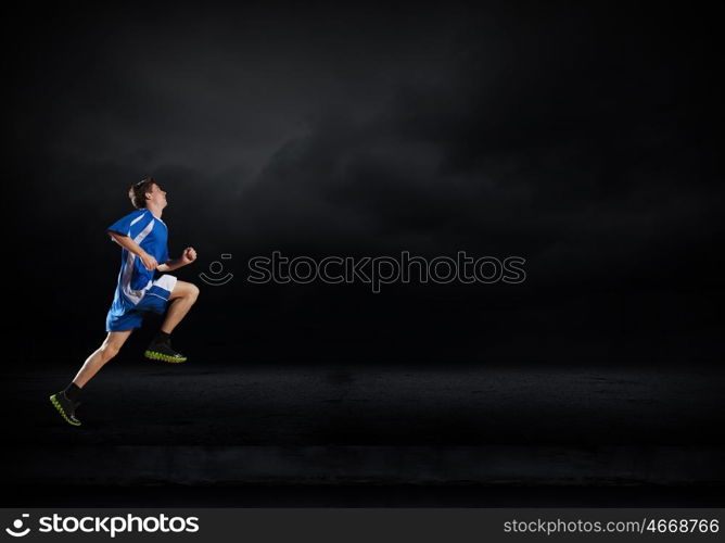 At full speed. Running man in blue sport wear on black background