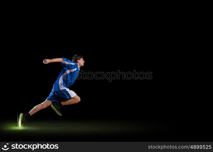 At full speed. Running man in blue sport wear on black background