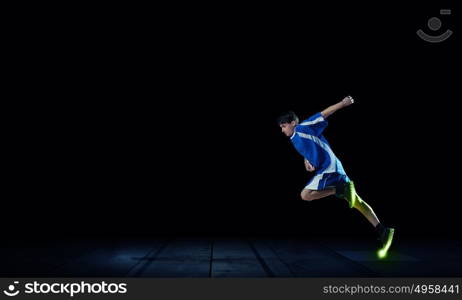 At full speed. Running man in blue sport wear on black background