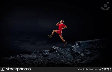 At full speed. Running man in red sport wear on dark background