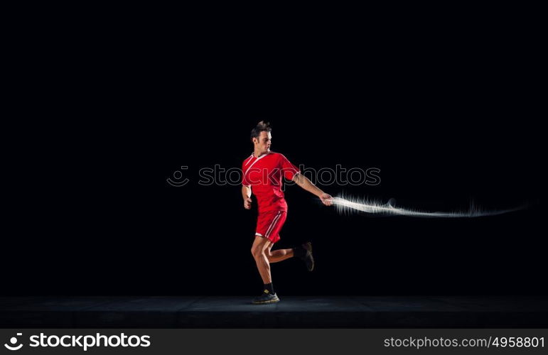 At full speed. Running man in red sport wear on dark background