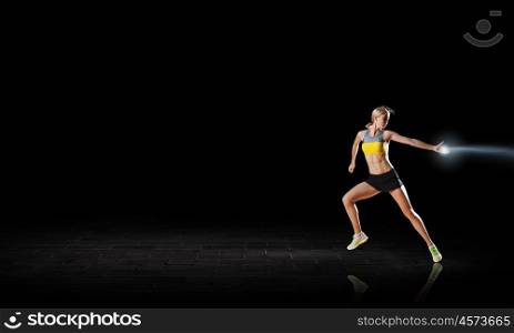 At full speed. Young woman athlete running fast on dark background