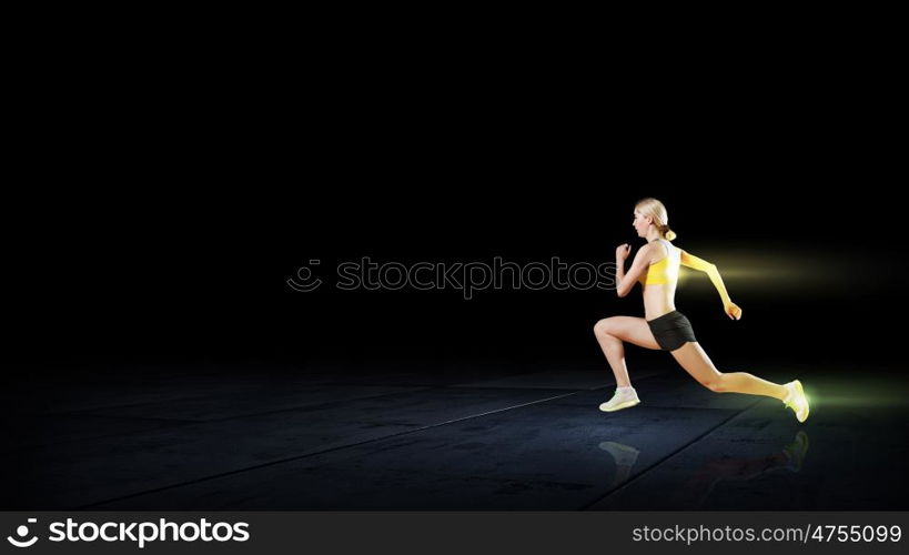 At full speed. Young woman athlete running fast on dark background