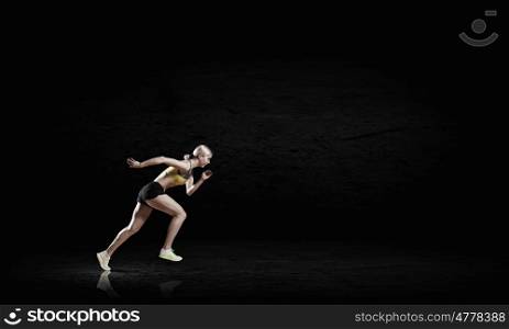 At full speed. Young woman athlete running fast on dark background