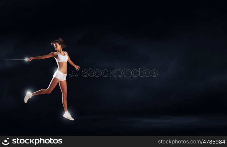 At full speed. Young woman athlete running fast on dark background