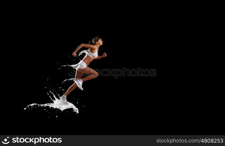 At full speed. Young woman athlete running fast on dark background