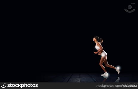 At full speed. Young woman athlete running fast on dark background