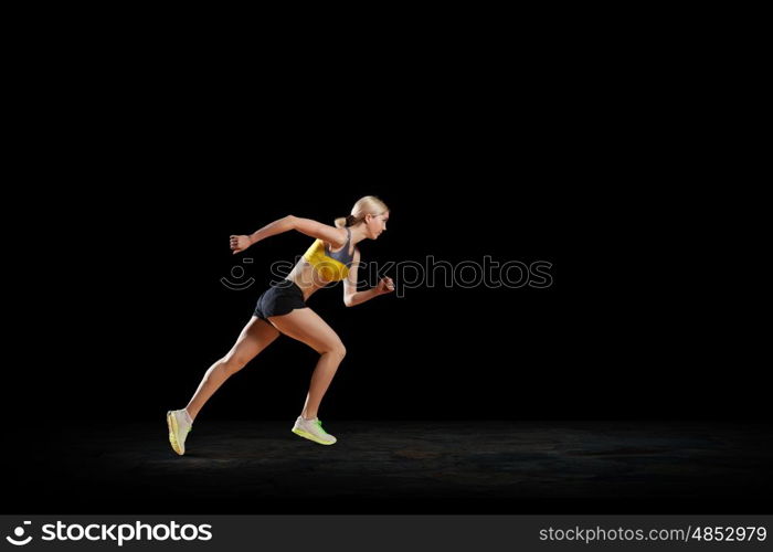 At full speed. Young woman athlete running fast on dark background