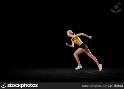 At full speed. Young woman athlete running fast on dark background