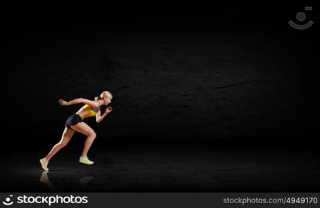 At full speed. Young woman athlete running fast on dark background