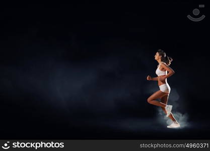 At full speed. Young woman athlete running fast on dark background