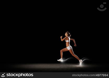 At full speed. Young woman athlete running fast on dark background