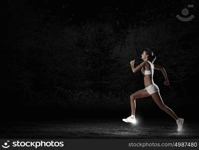 At full speed. Young woman athlete running fast on dark background