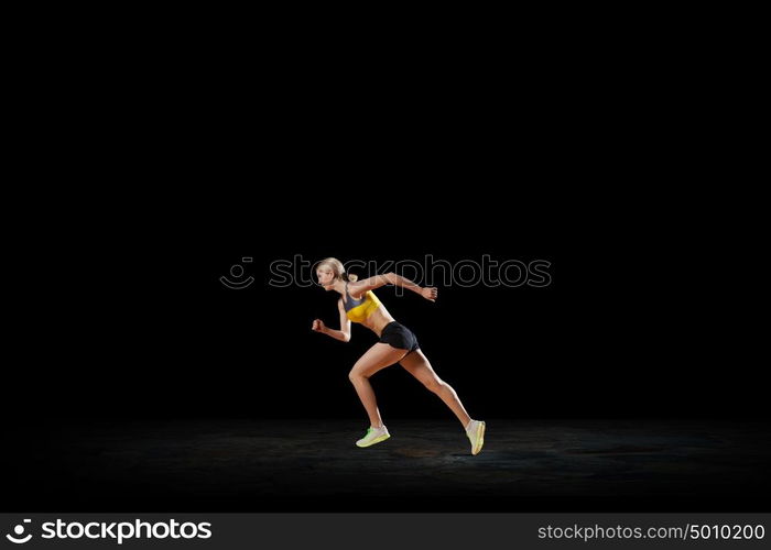 At full speed. Young woman athlete running fast on dark background