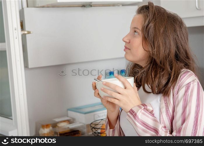 at morning, teenage girl is drinking coffee in a bowl