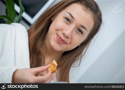 at morning, young and smiling woman eating a pastry