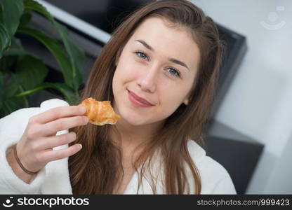 at morning, young and smiling woman eating a pastry