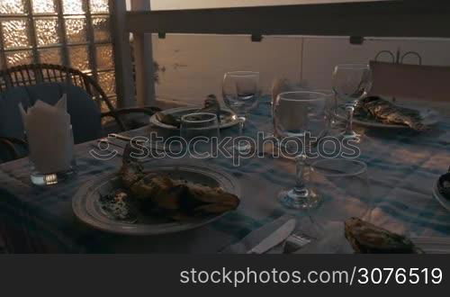 At sunset in city of Perea, Greece, dinner table served with cooked fish, snacks and glasses for wine. Seen beautiful sunset and coast of sea
